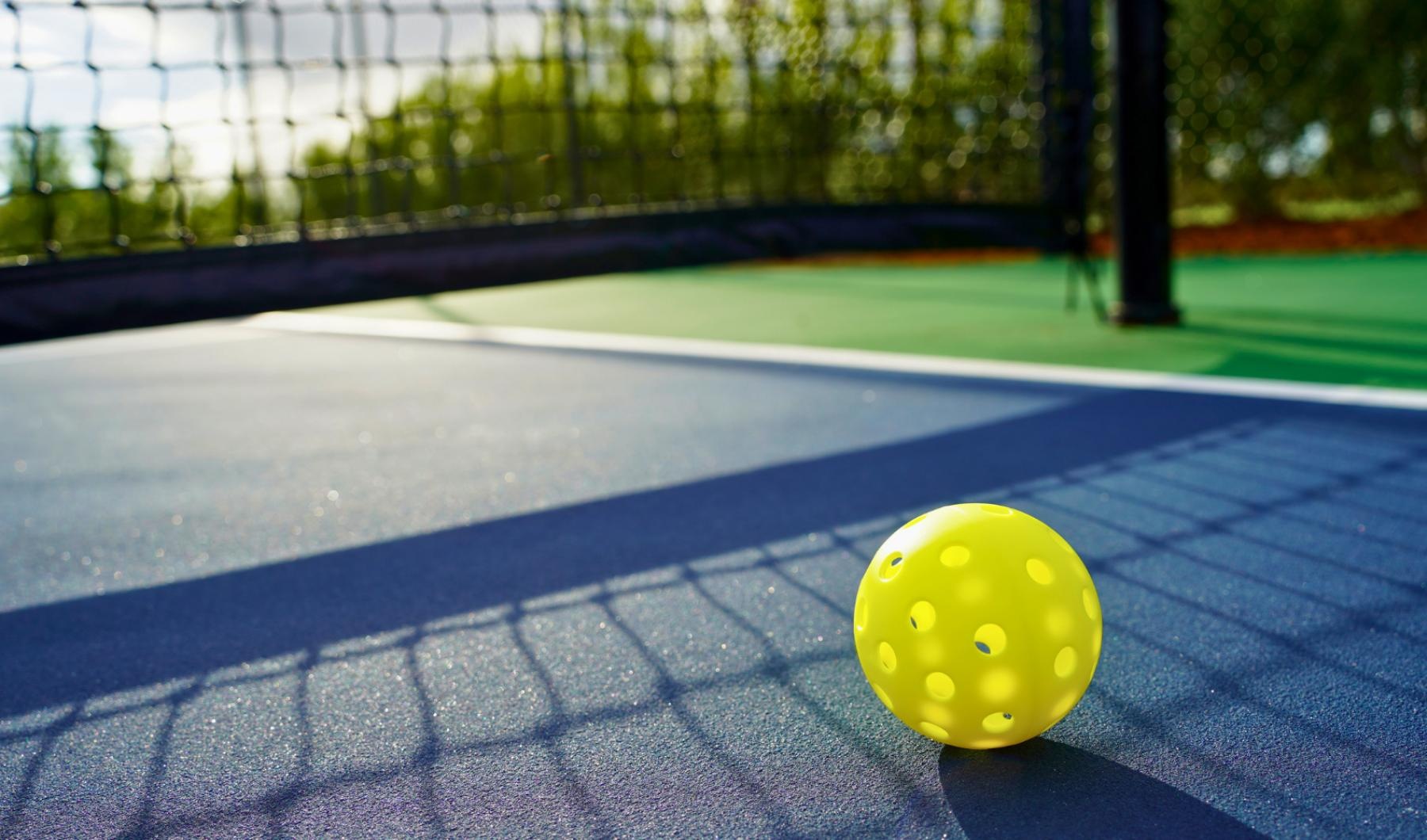 a yellow pickleball on a blue pickleball court